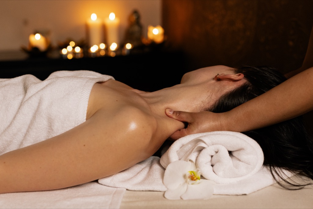 Aromaterapeutická masáž v&nbsp;salonu ESCAPE v&nbsp;Praze: terapeutka rukou s&nbsp;olejem uvolňuje šíji hostky, která leží na zádech s&nbsp;hlavou na srolovaném ručníku, v&nbsp;pozadí hoří svíčky